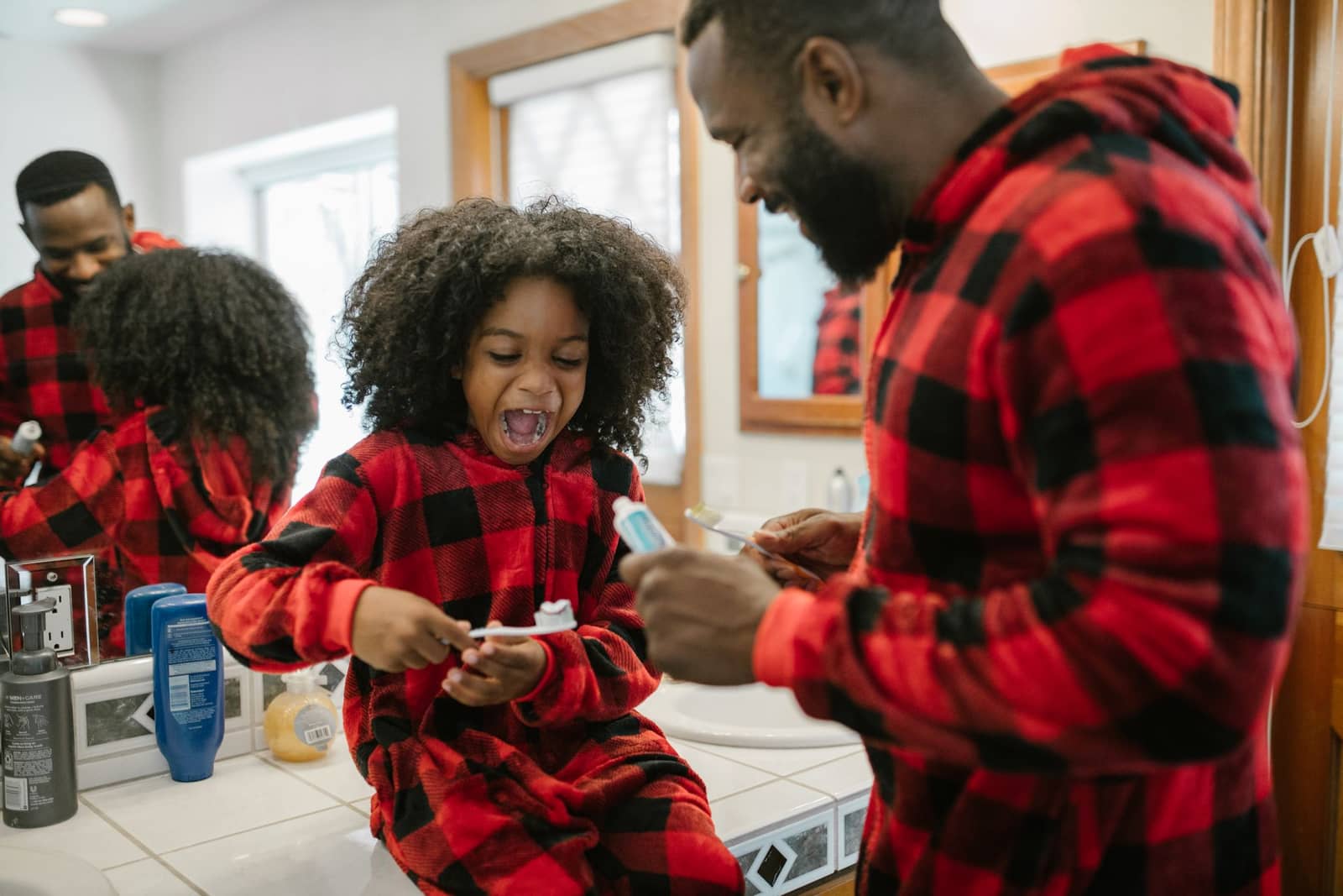 Father and daughter smiling while brushing their teeth