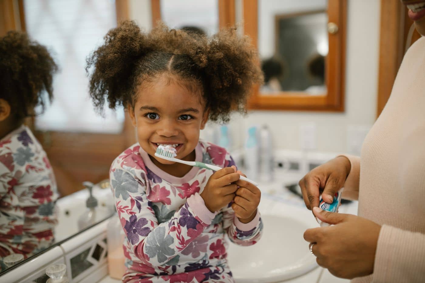 Young girl brushing her teeth with a parent nearby